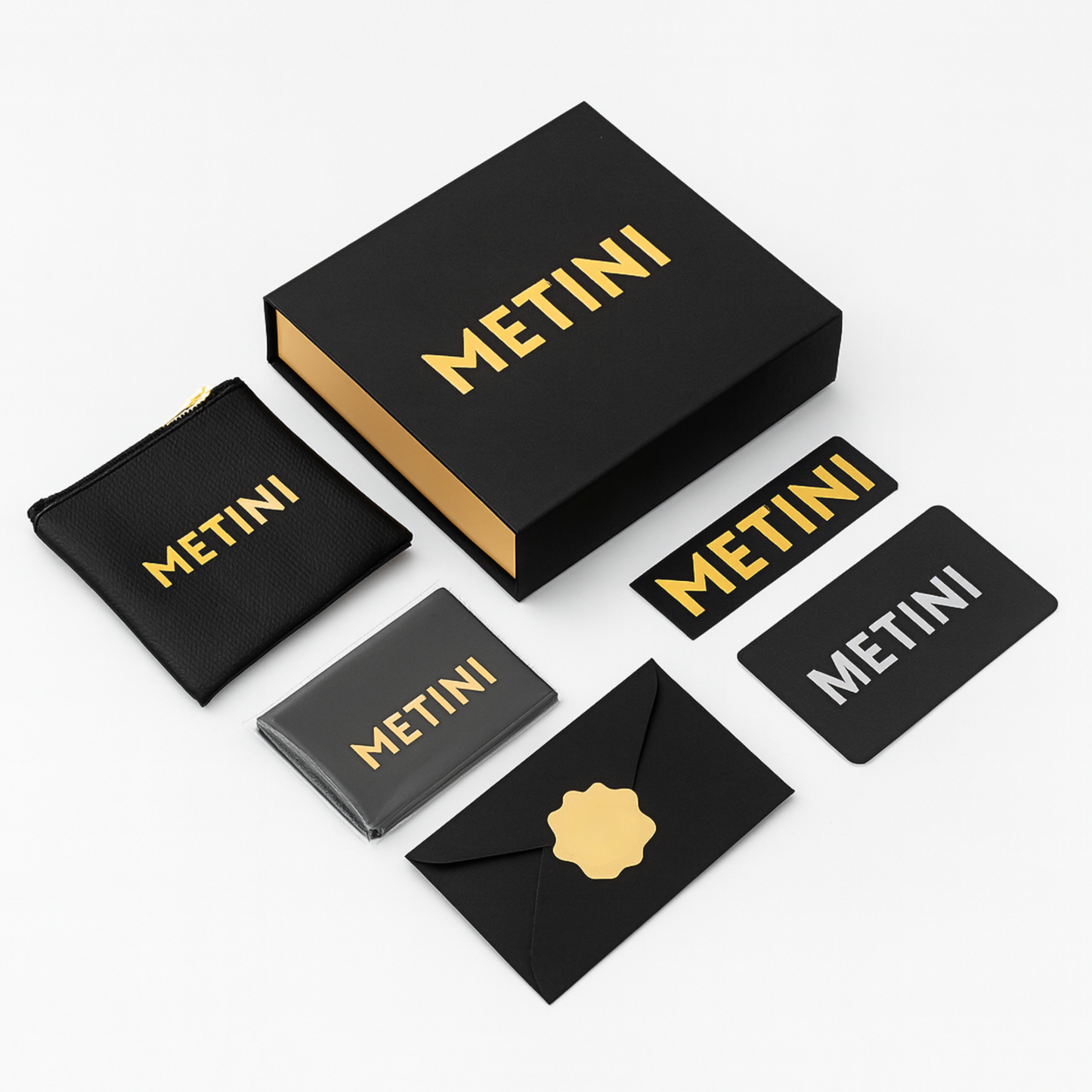 Opakowanie prezentowe METINI z czarnym pudełkiem, etui i elementami z logo w złotym kolorze: naklejka, koperta z kartą gwarancyjną, ściereczka z logo z mikrofibry i saszetka na suwak z ekoskóry.