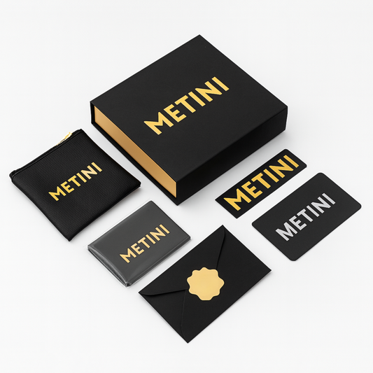 Opakowanie prezentowe METINI z czarnym pudełkiem, etui i elementami z logo w złotym kolorze: naklejka, koperta z kartą gwarancyjną, ściereczka z logo z mikrofibry i saszetka na suwak z ekoskóry.